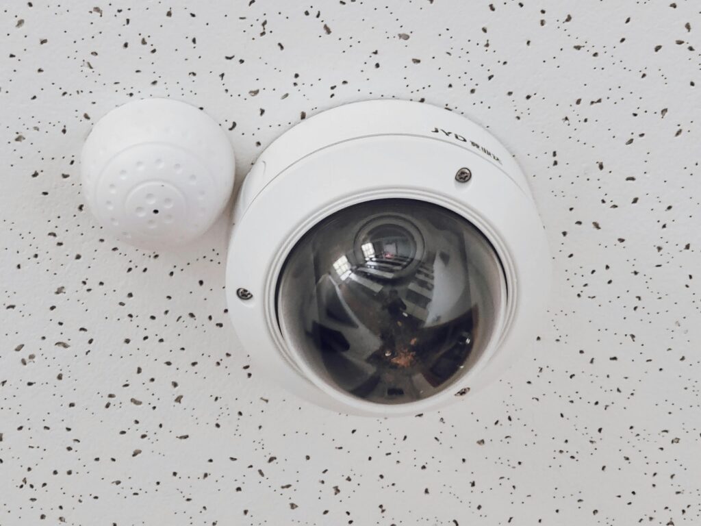 セキュリティー監視のため、まだら模様の天井に設置された丸型ドーム監視カメラのクローズアップ。